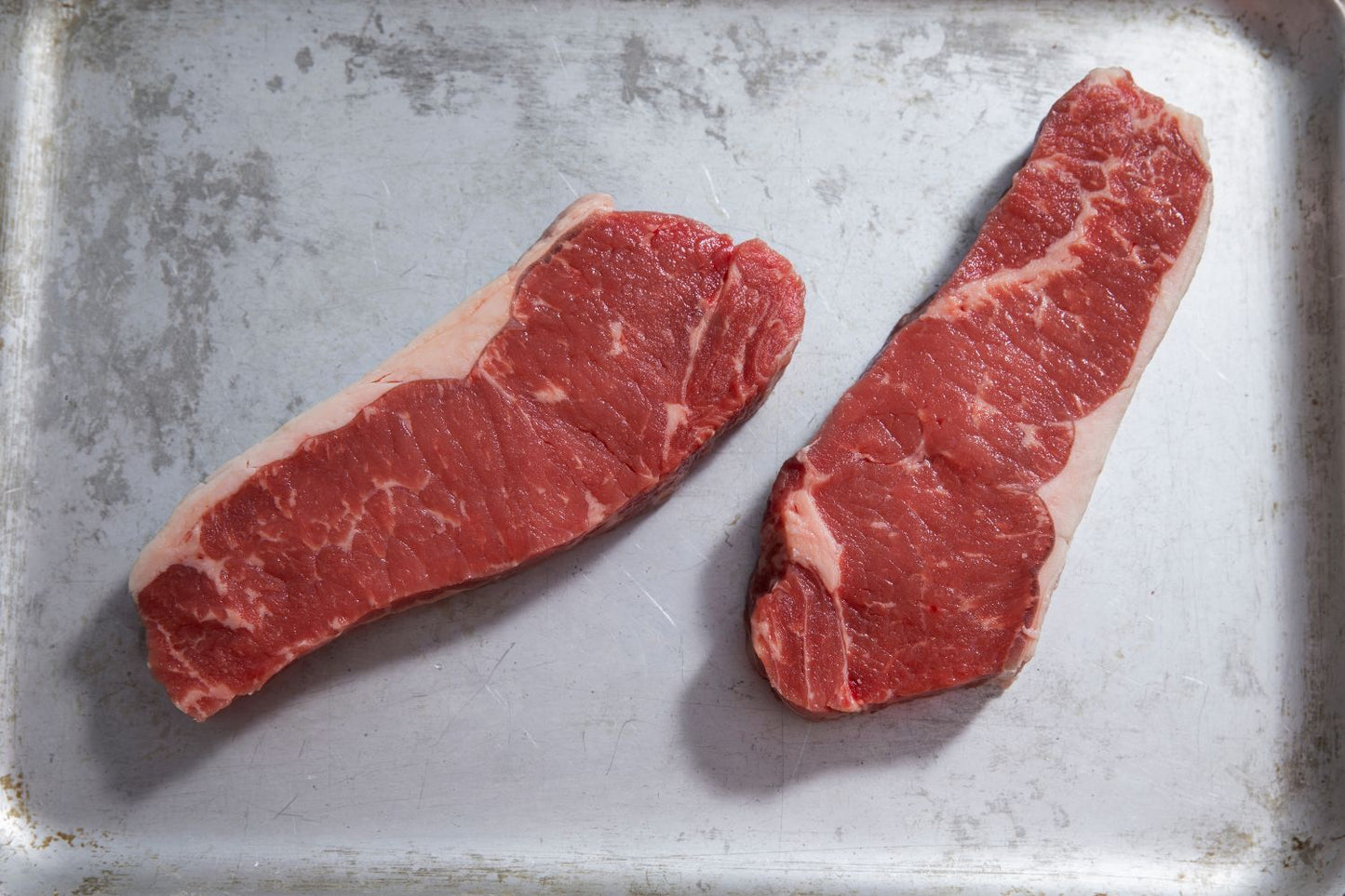 Two raw sirloin steaks on a metal tray