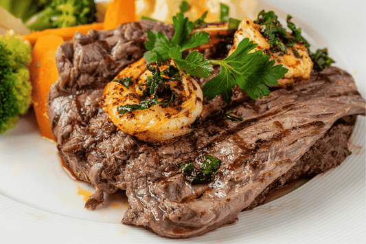 Steak with garlic marinated prawns and greens on a white plate